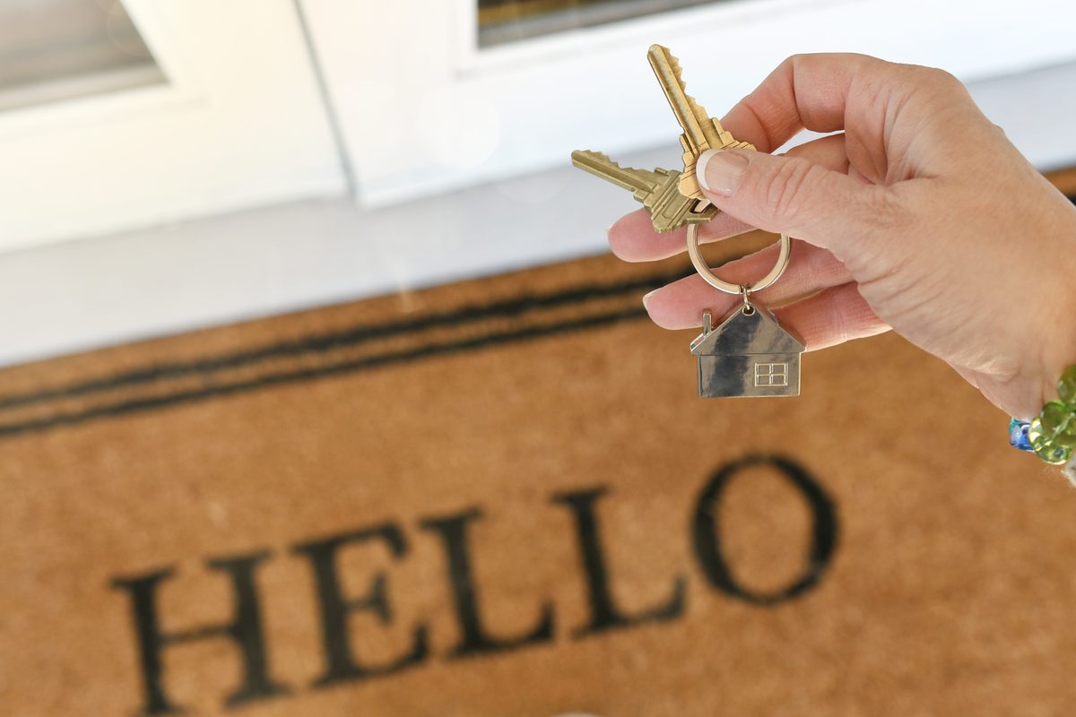 Hand holding house keys on a welcome doormat
